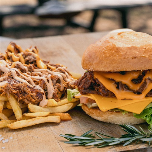 Fries with brisket and sauce next to a brisket burger on a wooden chopping board - Mr Pulled Slow Cooked Meats